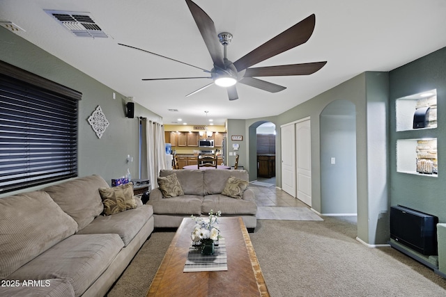 living area featuring visible vents, arched walkways, baseboards, light colored carpet, and ceiling fan