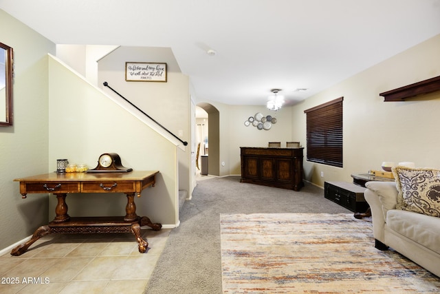 carpeted living room featuring stairway, arched walkways, baseboards, and tile patterned flooring