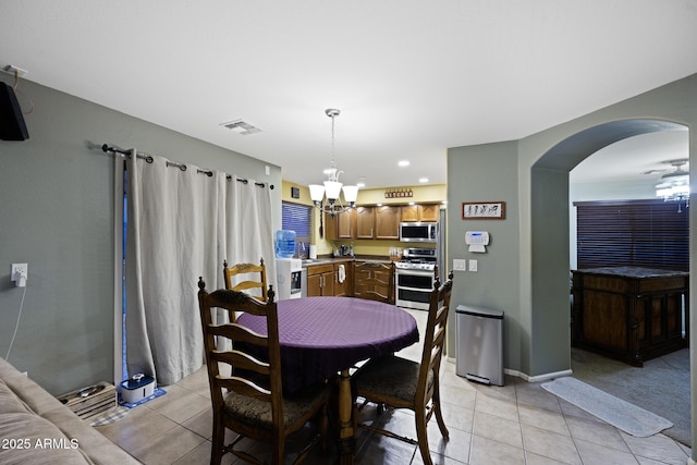 dining area featuring light tile patterned floors, visible vents, arched walkways, and an inviting chandelier