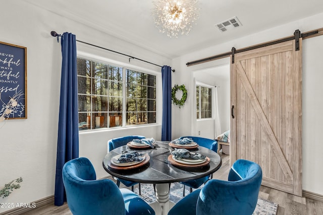 dining room featuring visible vents, a barn door, wood finished floors, a chandelier, and baseboards