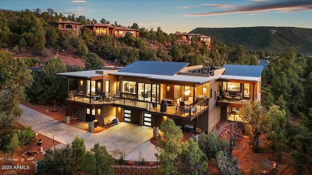 back of house at dusk with a garage, concrete driveway, and a balcony