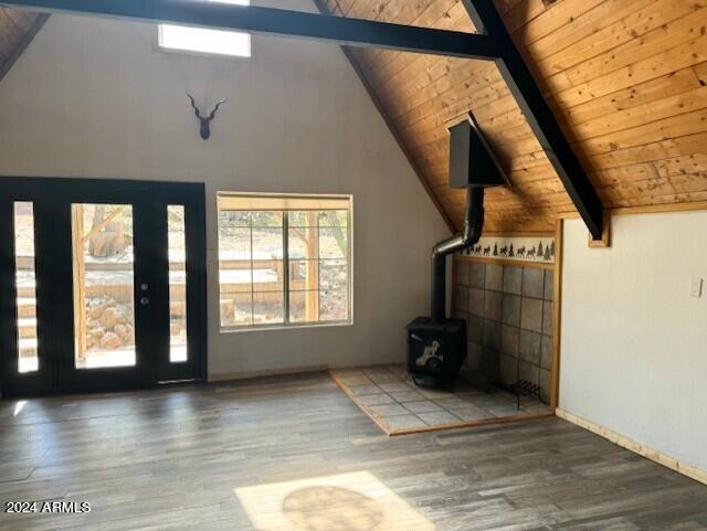 unfurnished living room with vaulted ceiling with beams, dark wood-type flooring, a wood stove, and wooden ceiling