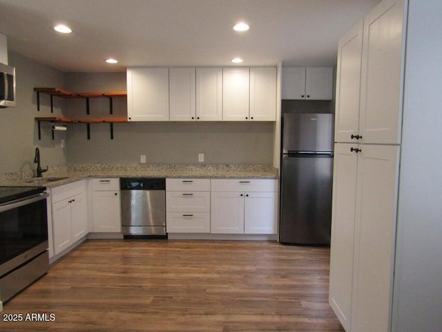 kitchen with white cabinets, appliances with stainless steel finishes, light stone counters, and dark wood-type flooring