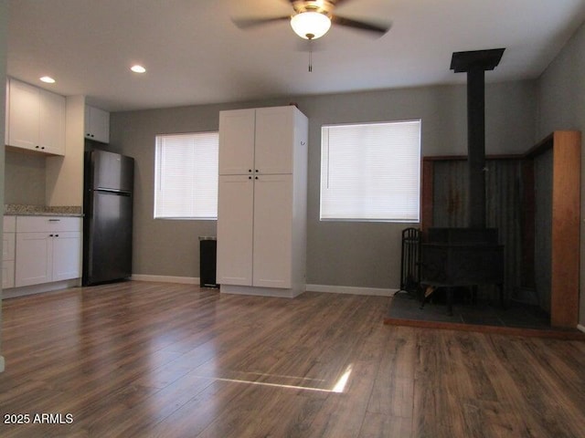 unfurnished living room featuring ceiling fan, dark hardwood / wood-style flooring, a wood stove, and a wealth of natural light