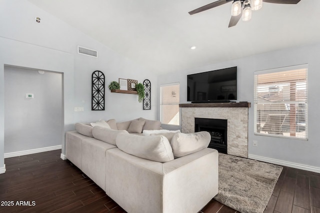 living room featuring ceiling fan, lofted ceiling, dark hardwood / wood-style floors, and a stone fireplace