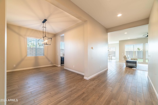 unfurnished dining area featuring ceiling fan with notable chandelier, a healthy amount of sunlight, and wood-type flooring