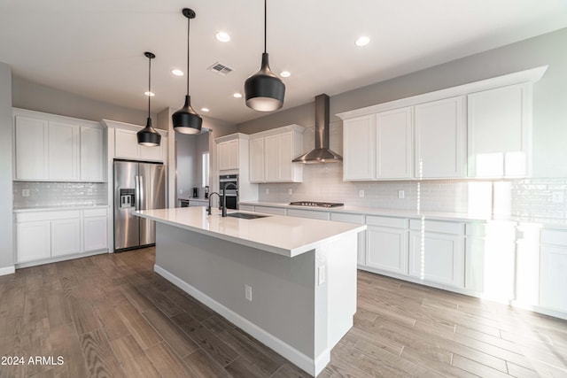 kitchen with white cabinets, stainless steel appliances, wall chimney exhaust hood, and light hardwood / wood-style floors