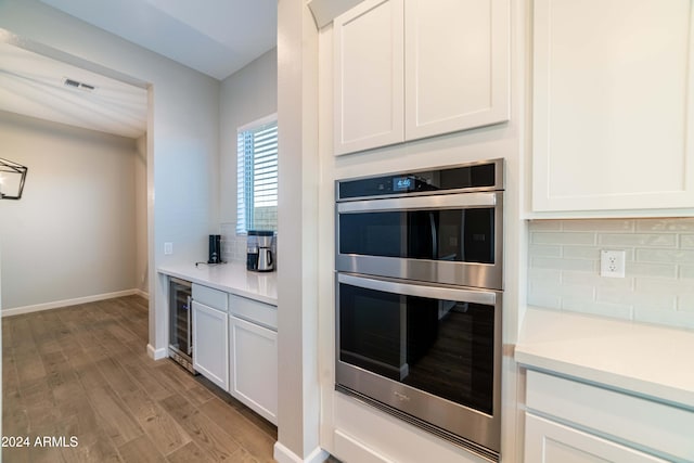 kitchen featuring double oven, wine cooler, white cabinets, and light wood-type flooring