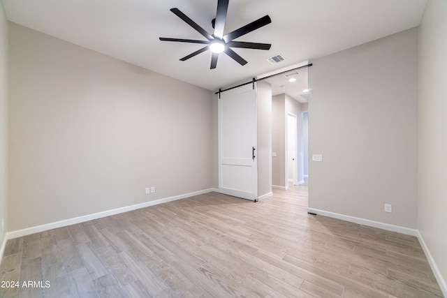 empty room with a barn door, ceiling fan, and light hardwood / wood-style floors