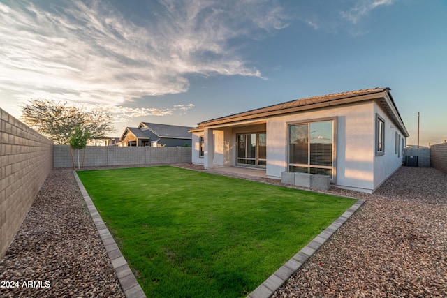 back house at dusk featuring a lawn