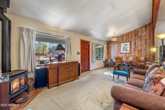 living room featuring vaulted ceiling, light carpet, a chandelier, wood walls, and a wood stove