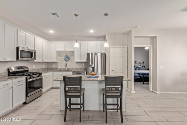 kitchen featuring appliances with stainless steel finishes, a center island, pendant lighting, light stone counters, and white cabinets