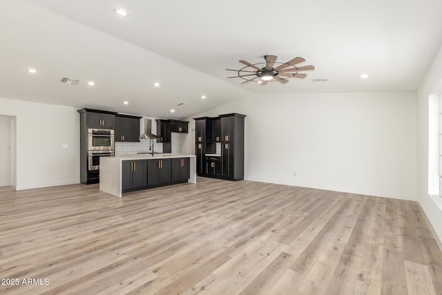 unfurnished living room with ceiling fan, sink, light wood-type flooring, and vaulted ceiling