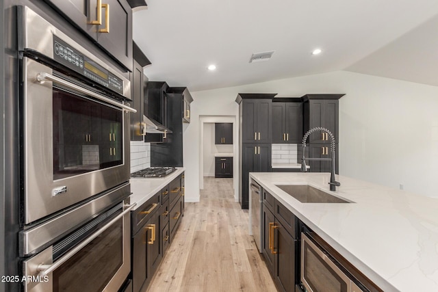 kitchen featuring lofted ceiling, stainless steel appliances, decorative backsplash, sink, and light wood-type flooring