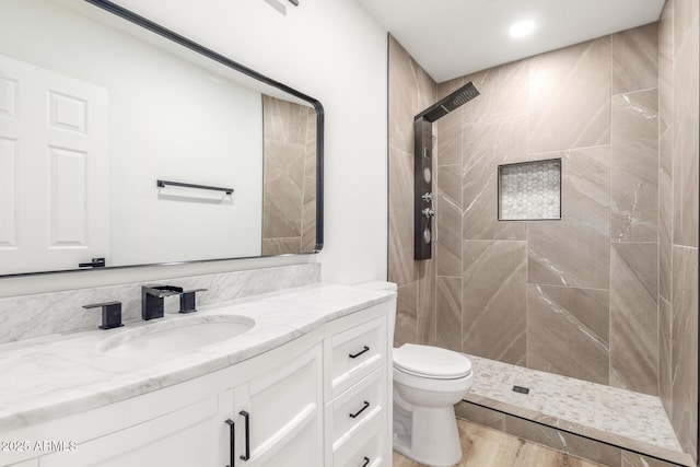 bathroom with toilet, tiled shower, hardwood / wood-style floors, and vanity