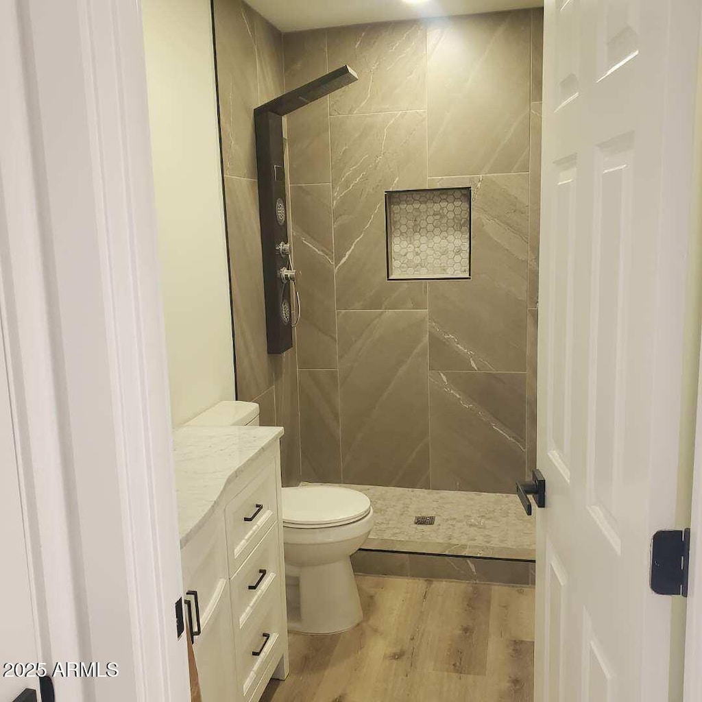 bathroom featuring wood-type flooring, toilet, tiled shower, and vanity