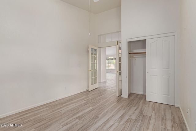 unfurnished bedroom featuring a high ceiling, a closet, french doors, and light hardwood / wood-style floors