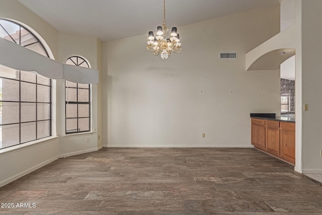 unfurnished dining area with a high ceiling, a notable chandelier, and dark hardwood / wood-style flooring