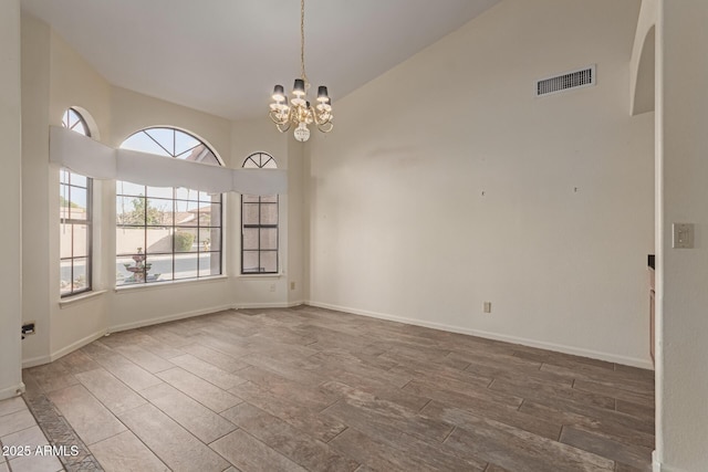 spare room featuring hardwood / wood-style floors, high vaulted ceiling, and a notable chandelier