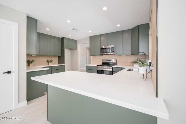 4506 W Golden Ln, Glendale, AZ 85302 - kitchen featuring backsplash, a peninsula, appliances with stainless steel finishes, and green cabinets