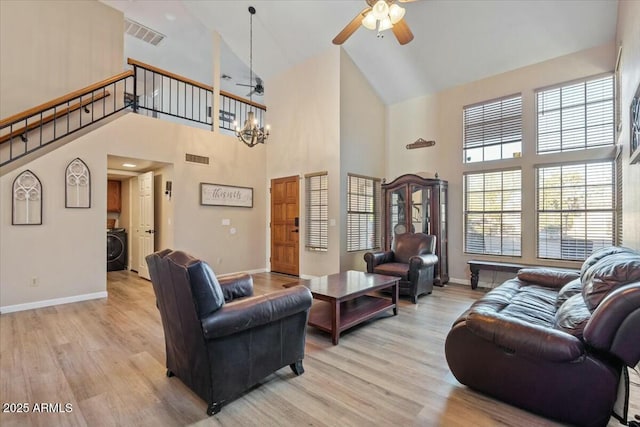 living room with ceiling fan with notable chandelier, washer / dryer, a towering ceiling, and light hardwood / wood-style flooring