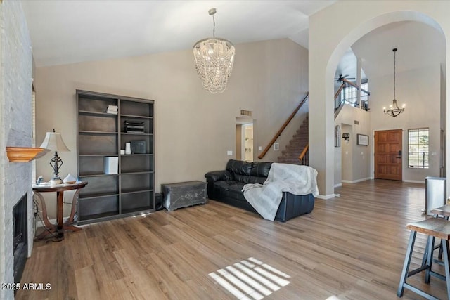 living room with wood-type flooring, high vaulted ceiling, a stone fireplace, and ceiling fan