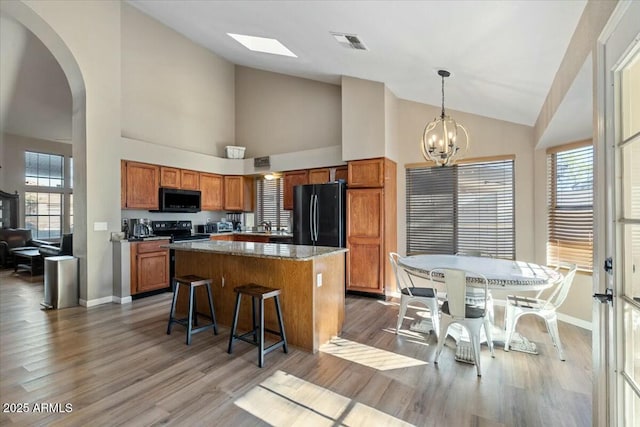 kitchen featuring a center island, an inviting chandelier, black appliances, hanging light fixtures, and a towering ceiling