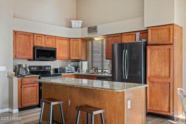 kitchen with light stone countertops, sink, light hardwood / wood-style flooring, a kitchen bar, and black appliances