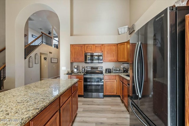 kitchen with light stone counters, stainless steel appliances, ceiling fan, light hardwood / wood-style flooring, and a high ceiling