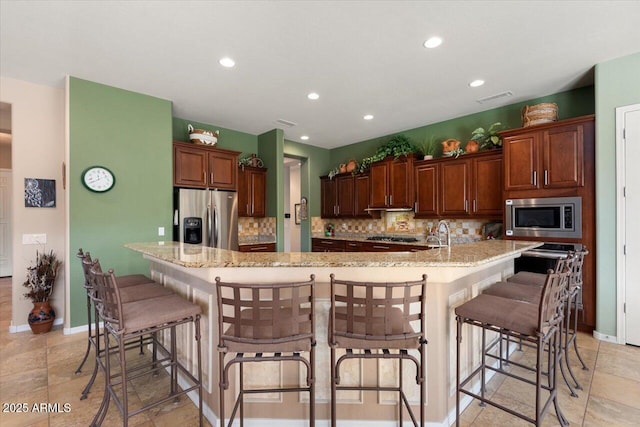 kitchen featuring stainless steel appliances, light stone counters, backsplash, a spacious island, and a kitchen bar