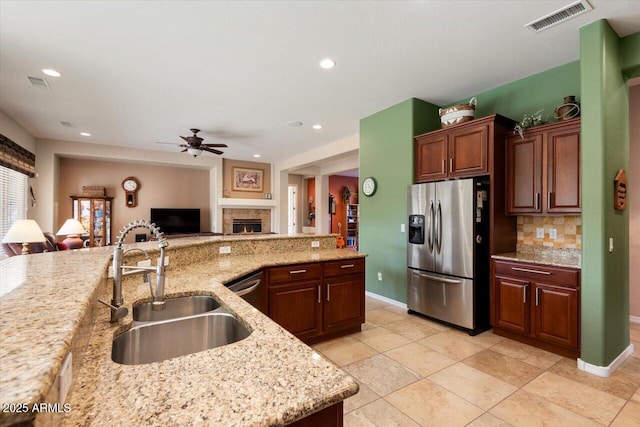 kitchen featuring backsplash, sink, ceiling fan, stainless steel fridge, and light stone counters