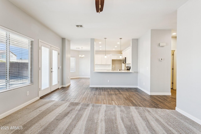 unfurnished living room featuring french doors, a notable chandelier, wood-type flooring, and a wealth of natural light