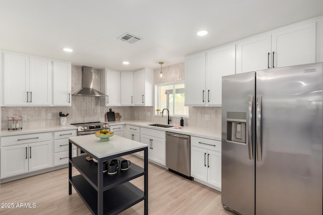 kitchen with stainless steel appliances, wall chimney range hood, a sink, backsplash, and white cabinets