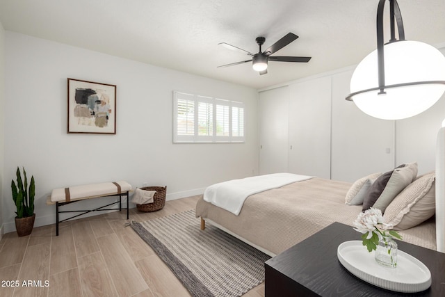 bedroom with light wood-style floors, a closet, baseboards, and a ceiling fan