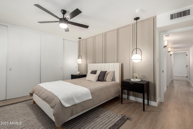 bedroom featuring light wood-type flooring, a decorative wall, a closet, and ceiling fan
