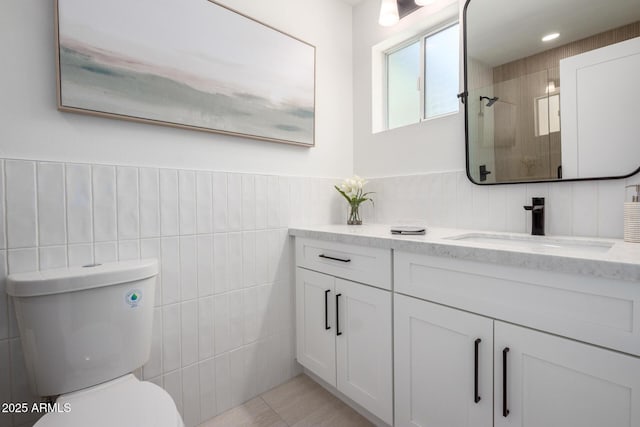 full bath featuring tile walls, toilet, a shower, vanity, and a wainscoted wall