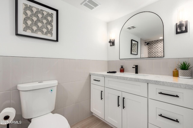 full bath featuring tile walls, toilet, vanity, a shower, and wainscoting