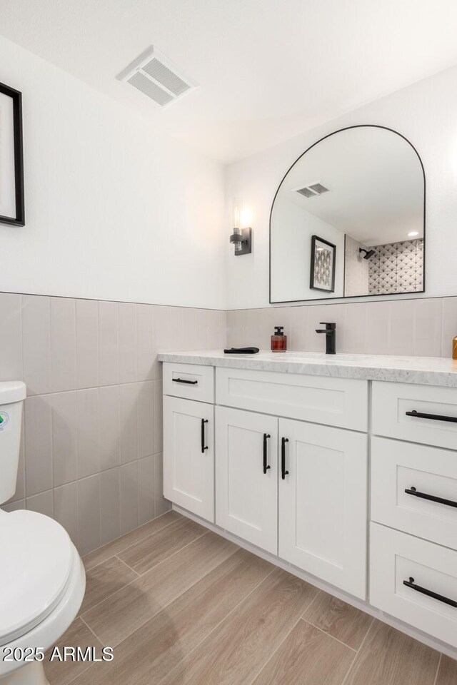 full bath with tile walls, toilet, vanity, and a shower