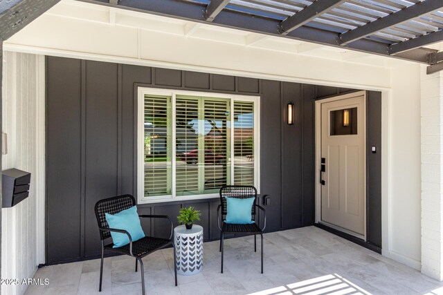 property entrance with board and batten siding, a pergola, and a patio area