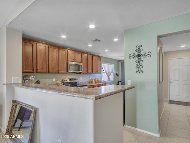 kitchen with light tile patterned floors, a peninsula, visible vents, appliances with stainless steel finishes, and brown cabinetry