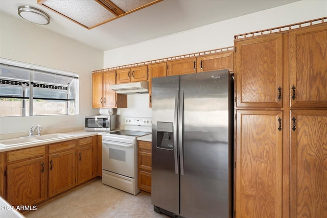 kitchen with brown cabinetry, light countertops, under cabinet range hood, a sink, and appliances with stainless steel finishes
