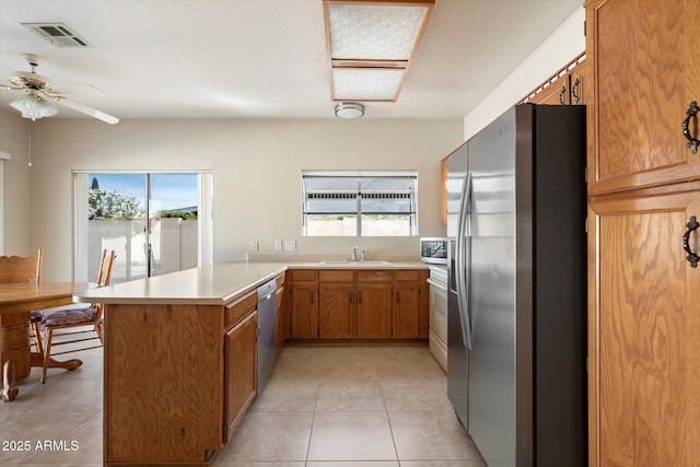 kitchen with visible vents, a peninsula, brown cabinets, a sink, and stainless steel appliances