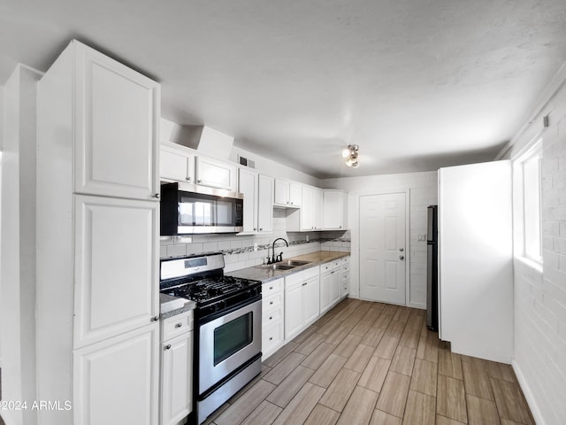 kitchen with appliances with stainless steel finishes, light hardwood / wood-style flooring, sink, and white cabinetry