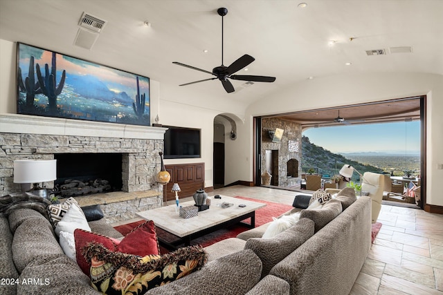 living room with ceiling fan, a stone fireplace, and vaulted ceiling