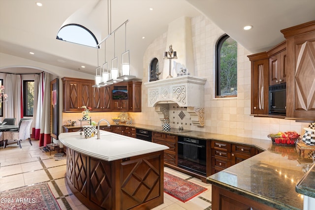 kitchen featuring decorative light fixtures, an island with sink, black appliances, decorative backsplash, and sink