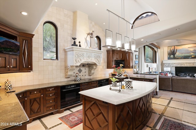 kitchen featuring light stone counters, hanging light fixtures, black appliances, decorative backsplash, and a kitchen island