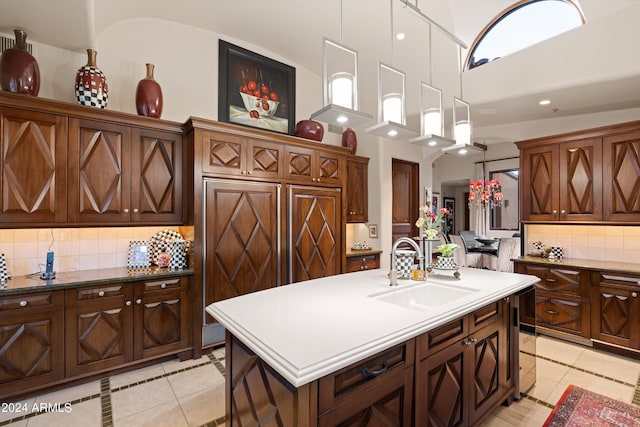 kitchen with sink, light tile patterned flooring, an island with sink, backsplash, and hanging light fixtures