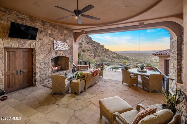 patio terrace at dusk featuring ceiling fan, a mountain view, and an outdoor living space with a fireplace