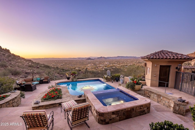 pool at dusk featuring outdoor lounge area, an in ground hot tub, a mountain view, and a patio area