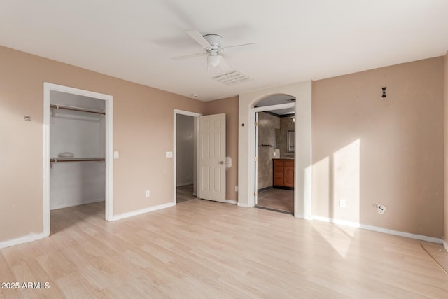 unfurnished bedroom with ensuite bathroom, a spacious closet, light wood-type flooring, a closet, and ceiling fan